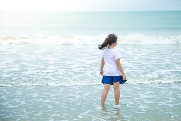Fototapeta na wymiar Asian girls Wearing a white shirt, blue pants Stand looking at the white waves in the blue sea