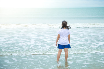Fototapeta na wymiar Asian girls Wearing a white shirt, blue pants Stand looking at the white waves in the blue sea