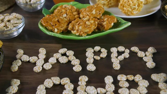 Tilt shot of 'Happy Lohri' text written with rewri on the harvest festival - Lohri. Closeup shot of 'Happy Lohri' surrounded by Lohri items like peanuts chikki  rewri  murmura ladoo  bhujia chikki ...