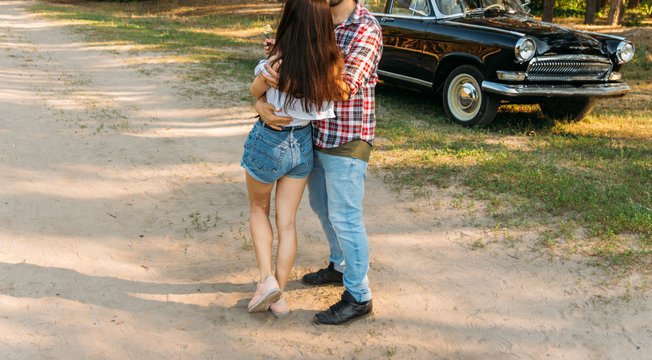 a couple standing hugs against the backdrop of a black car, a man leaning on the car door.vertical photo