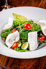 Spanish cuisine. Mixed salad fish salad, spinach, quail eggs, canned mackerel, olives, seasoned with olive oil, sesame and rice chips. Beautiful restaurant serving in a white plate