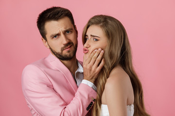 woman want to kiss her boyfriend and he does not want on pink background. man refuses kiss from girlfriend, shows stop gesture
