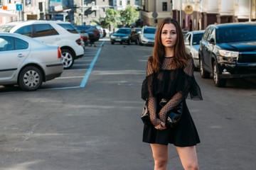 Fototapeta premium portrait of a girl, brunette, in a black dress, in the arch, in the city. posing, walking. alone in the crowd, loneliness.sad