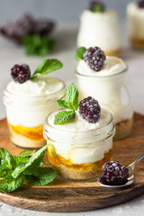 Homemade no baked dessert (cheesecake, trifle, mousse) with orange or peach jam in small portioned jars served with frozen berries and mint. Light grey stone background, copy space.