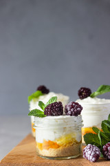 Homemade no baked dessert (cheesecake, trifle, mousse) with orange or peach jam in small portioned jars served with frozen berries and mint. Light grey stone background, copy space.