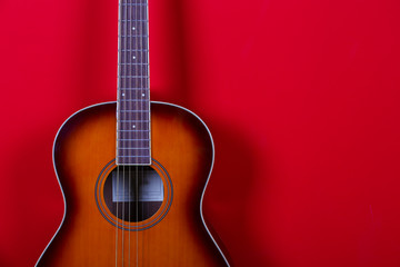 Obraz na płótnie Canvas Cropped image of vintage style travel size acoustic guitar with rosewood neck and no pickguard over festive red wall background. Close up, copy space for text, top view.