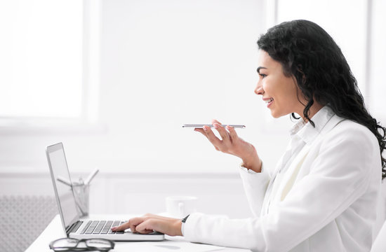 Cheerful hispanic secretary using voice assistant on cellphone