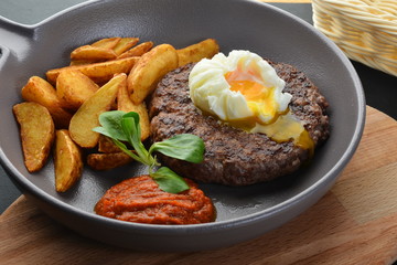 Beef steak with potatoes, poached sauce and poached egg, in a pan, large. Appetizing photo. Horizontal.