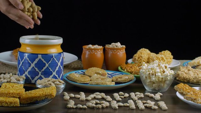 Closeup shot of woman hands pouring groundnuts in a beautiful clay jar - Lohri festival. Beautifully plated Lohri items with 'Happy Lohri' text written with rewri surrounded by til patti  gajak  po...