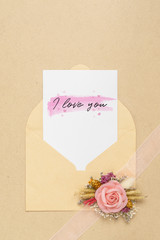 Mockup card and envelop on white wood with I love you text and kraft roses for Valentine's Day. Mock up for elegant design. Flat lay top view valentine's day background concept.