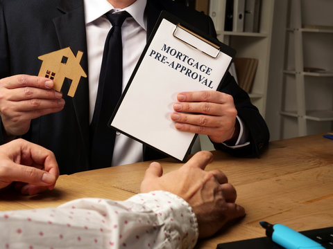 Realtor holds Mortgage Pre-Approval agreement form and model of house.
