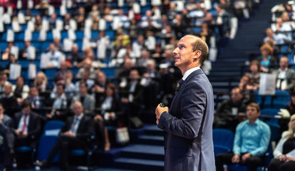 Speaker giving a talk on corporate business conference. Unrecognizable people in audience at...
