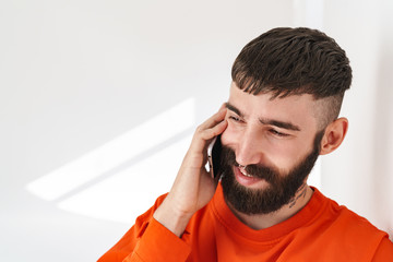 Image of young man talking on smartphone while standing over white wall