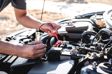 Mechanic repairman checking engine automotive in auto repair service and using digital multimeter testing battery to measure various values and analyze