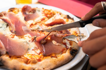 hand use knife and fork to slice homemade salami pizza, Italian food