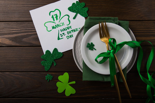 St Patrick's Day party table setting decorated with green leprechaun on wooden background.