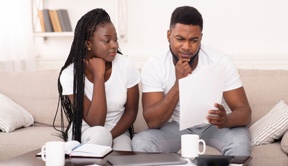 Black married couple reading papers sitting on couch at home