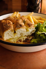 Grilled Focaccia bread sandwich filled with melted cheese sausage and served with French fries and salad