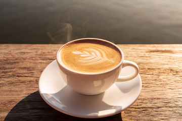 Close up a coffee latte in white cup and milk froth above to drink on brown wooden table background, increase energy for today