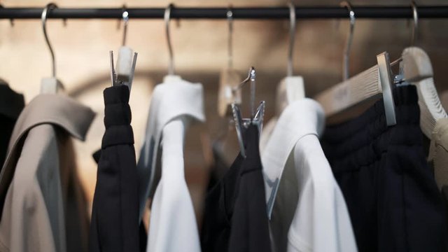 Close up pan shot left to right of designer clothes hangers with black, beige, white clothes on a hanger. Showroom of new casual clothes on a hanger in a shop