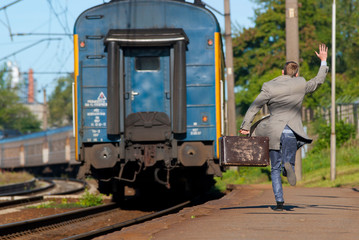 A man is trying to catch a train. Man is late for train. Man is running behind a train and waving his hand. 