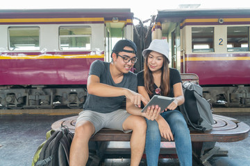 Young asian couple backpacker using tablet for find destination trip at railway station