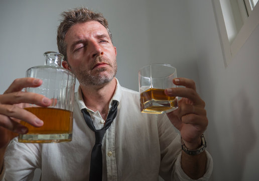 portrait of 30s to 40s alcoholic  man in lose necktie drinking desperate holding whiskey glass thoughtful drunk and depressed completely wasted in alcohol addiction concept