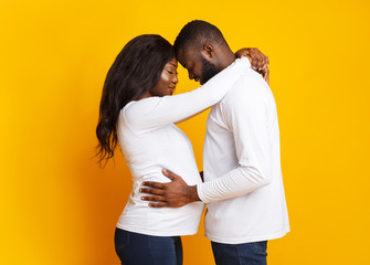 Young married couple cuddling over yellow background