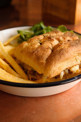 Grilled Focaccia bread sandwich filled with melted cheese sausage and served with French fries and salad