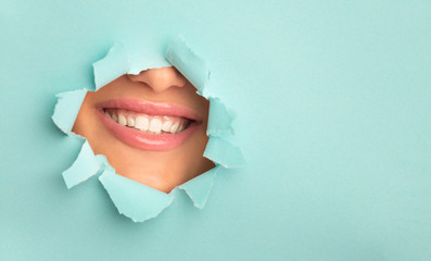 Woman with broad smile, peep through turquoise torn paper