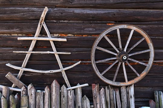 Vintage wooden triangular drying rack and wagon wheel hanged on wall of blockhouse behind plank fence