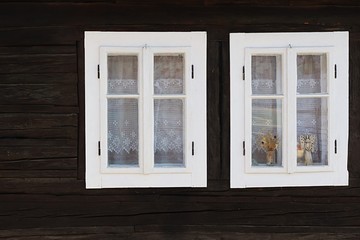 Two wooden windows with white painted window frame on the wall of historical blockhouse in northern Slovakia. Some decorations are placed between inner and outer frame of right window. 