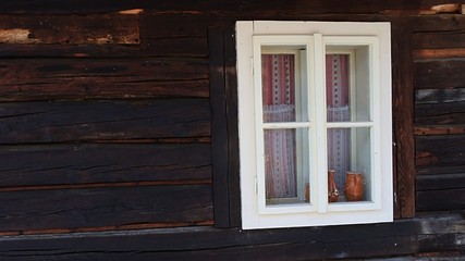 Antique wooden window with white painted window frame on the wall of historical blockhouse in northern Slovakia. Some creamic pots and vases are placed as decoration behind window frames. 