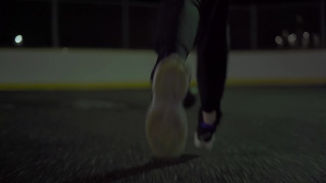Female running with black pants to get a basketball on an outdoor court in the dark with wet pavement.