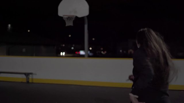 Girl runs towards basketball net at night and shoots far shot in.