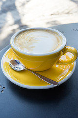 A yellow cup of coffee on the table. A fresh morning coffee time in downtown street cafe.  