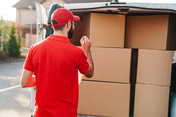 Image of young delivery man holding clipboard and counting parcel boxes