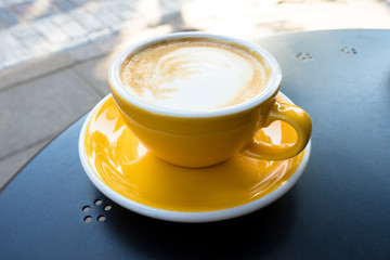 A yellow cup of coffee on the table. A fresh morning coffee time in downtown street cafe.  