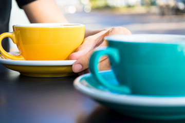 A yellow cup of coffee on the table. Young woman drinks fresh morning coffee in downtown street cafe.  