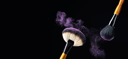 Makeup concept with a  professional makeup brushes with glowing purple eye shadow isolated on black background.