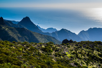 Spain, Tenerife, Wide view over blue ocean horizon and boats from cliffy green mountains of masca canyon on sunny day
