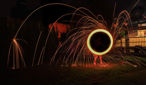 a long exposure photography of an steel wool on fire going in circles and dropping iron on fire as a shower