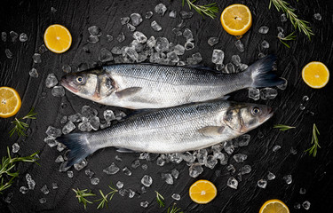 Obraz na płótnie Canvas Seabass fish on ice on black stone background, top view