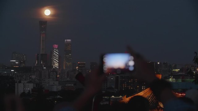 Tourists taking pictures of the full moon in the beautiful scenery of Beijing's skyscrapers