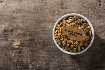 Sunflowers seeds in white bowl on wooden table. Top view. Copy space