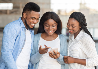 Millennial afro girl showing funny content on smartphone to friends