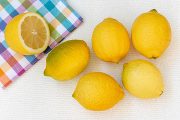 Cinco limones sobre un fondo blanco y medio limón sobre un paño de cocina con cuadrados de colores