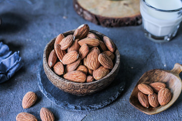Photo of almond in wooden bowl on gray background. Almond with wooden spoon or scoop. Raw whole almond. Almond milk. Images
