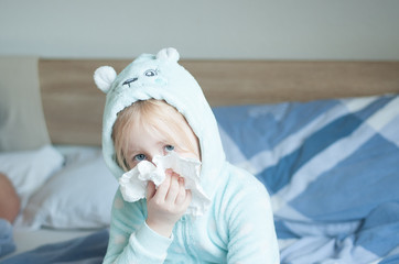 child with cold symptoms in a blue cute home jumpsuit on a large bed