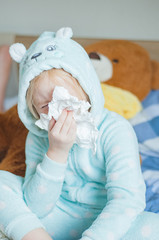 child with cold symptoms in a blue cute home jumpsuit on a large bed